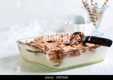 Eislöffel und hausgemachtes Schokoladen- und Vanilleeis in einem Glasbehälter Stockfoto