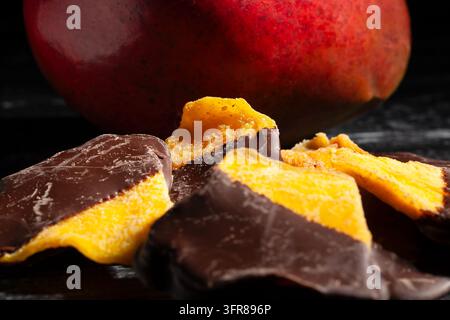 Schokoladengetaufter Mango auf schwarzem Holzgrund Stockfoto