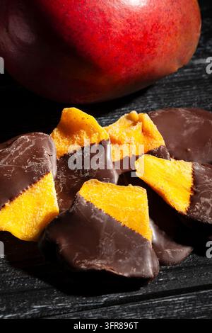 Schokoladengetaufter Mango auf schwarzem Holzgrund Stockfoto