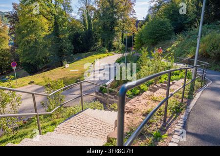 Eine Treppe mit Metallgeländern führt hinunter zu einem kurvenreichen Weg im sonnigen Park, Calw Stadtgarten, Landkreis Calw, Deutschland Stockfoto