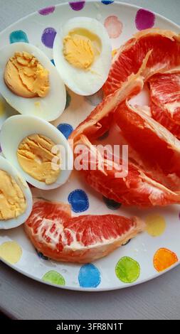 Gekochte Eier und Grapefruitscheiben auf einem bunten Teller Stockfoto