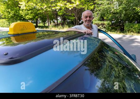 Taxifahrer lehnt sich auf das Dach seines Autos mit einem gelben Taxischild, Provinz Shirak, Gjumri, Armenien Stockfoto