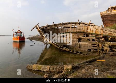 Ein kleines Fischerboot schwebt neben dem verfallenden Rumpf eines verlassenen Holzschiffs bei Ebbe, Gujarat, Mandvi, Indien Stockfoto