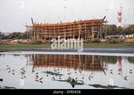Ein riesiges Holz-Dhow im Bau steht auf Pfählen, während eine Vogelschar über ihm fliegt, Gujarat, Mandvi, Indien Stockfoto