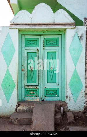 Eine verwitterte Holztür, die mintgrün gestrichen ist, steht in einer diamant gemusterten Wand, Gujarat, Mandvi, Indien Stockfoto