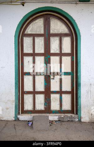 Verwitterte braune hölzerne gewölbte Doppeltür mit grünem Rahmen und abblätternder Farbe, Gujarat, Mandvi, Indien Stockfoto