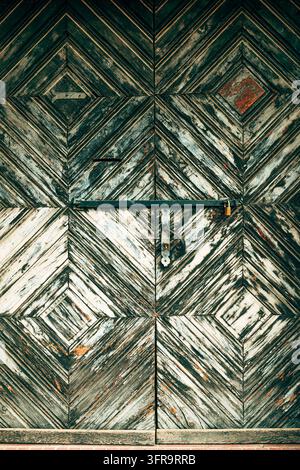 Frontalansicht von kunstvollen antiken hölzernen Doppeltüren mit einem geometrischen Rautenmuster und metallener Verriegelung. Vertikale Aufnahme. Stockfoto