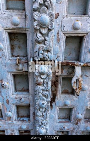 Nahaufnahme einer hellblauen antiken Tür mit abblätternder Farbe, einem geschnitzten floralen Mittelpfosten und einem rostigen Eisenschlossriegel in vertikaler Komposition auf abgenutzter Platte Stockfoto