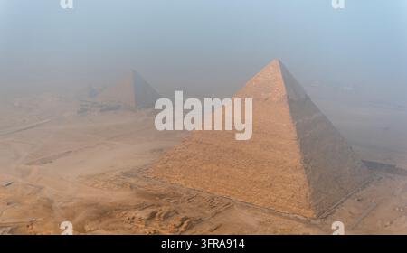 Luftaufnahme der Nekropole von Gizeh mit der Großen Pyramide von Gizeh und anderen Pyramiden, die aus der Wüstenlandschaft unter einem dunstigen Himmel in Al Haram, Gizeh, aufragen Stockfoto
