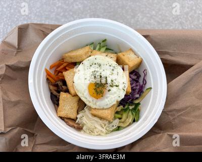 Frischer Tofu-Bibimbap zum Mitnehmen, serviert in einer weißen Schüssel, mit gebratenem Tofu, Gemüse, gebratenem Ei und gemischtem Gemüse über Reis. Stockfoto