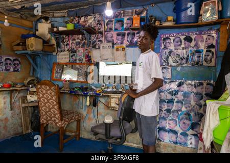 Ein junger Mann steht in einem Friseursalon, der mit Frisurenpostern geschmückt ist, Maritime Region, Lome, Togo Stockfoto