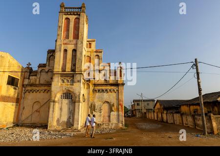 Zwei Männer gehen an einer alten Kolonialkirchenfassade vorbei, die in goldenem Licht badet, Maritime Region, Aneho, Togo Stockfoto