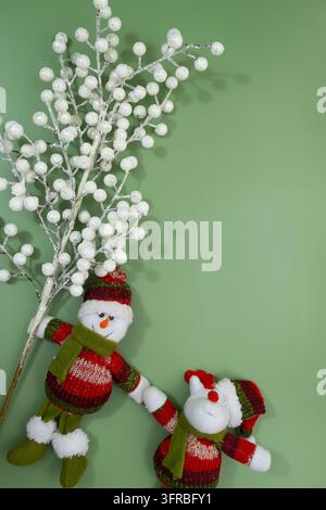 Schneemann- und Rentier-Weihnachtsfiguren mit weißen Winterbeeren auf einem grünen Hintergrund Stockfoto