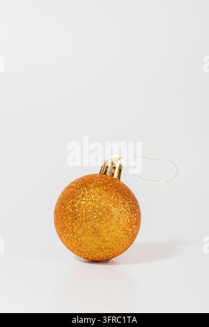 Goldener Glitzerball schimmert sanft vor einem sauberen weißen Hintergrund. Seine funkelnde Oberfläche fängt Licht ein und strahlt Wärme und Freude aus. Zarter Drahtring deutet an Stockfoto