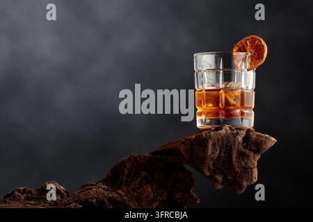 Altmodischer Cocktail mit Eis und einer getrockneten Orangenscheibe, serviert auf verwittertem Treibholz. Whiskey mit Bitter und Eis. Kopierraum. Stockfoto
