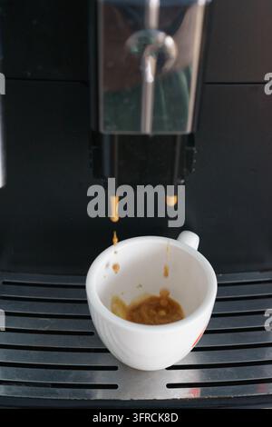 Nahaufnahme einer Espressomaschine, die Kaffee in eine kleine weiße Keramiktasse ausschenkt, und fängt den Kaffeezubereitungsprozess in einer modernen Kaffeemaschine ein. Stockfoto