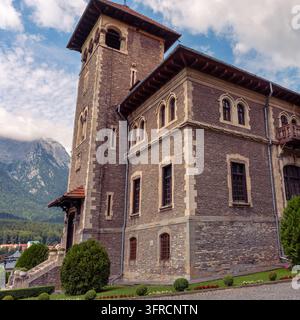 Hoher Steinturm und gewölbte Fenster des Cantacuzino-Schlosses vor einem wolkigen blauen Himmel in Buşteni, Rumänien Stockfoto