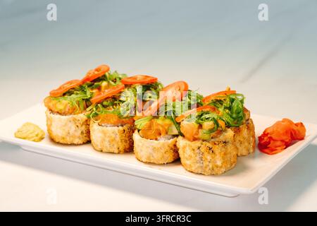 Knusprig gebratene Sushi-Rollen, garniert mit Lachs, Algensalat und Kirschtomaten, werden mit Wasabi und Ingwer eingelegt serviert. Stellt japanisches Fusion-Cuisine dar Stockfoto