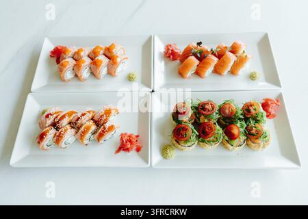 Vier Teller mit verschiedenen Sushi-Rollen mit Lachs, Fischrogen, Algen-Salat und Soßen sind auf einem Tisch arrangiert. Stellt japanisches Essen, Catering, Foo dar Stockfoto
