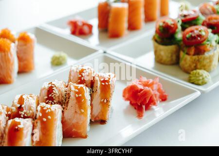 Verschiedene Sushi-Rollen mit gebratenem Lachs, Sesamdressing und Algen-Salat werden auf weißen Tellern präsentiert. Stellt japanische Fusion-Küche dar, Restaurant Stockfoto