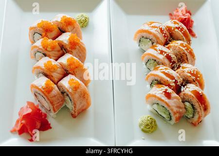 Zwei Teller mit gebratenen Lachs-Sushi-Rollen, gekrönt mit orangefarbenem Fischrogen und Sesamsauce, werden mit Wasabi und Ingwer serviert. Repräsentiert japanische Ku Stockfoto