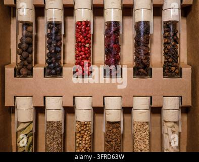 Nahaufnahme von verschiedenen ganzen Gewürzen in Glasampullen, die in einer Pappgeschenkbox angeordnet sind, mit Zimt, Kardamom, Nelken, Pfefferkörnern und anderen aromatischen Gewürzen Stockfoto