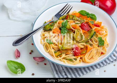 Linguini-Pasta mit Zucchini- und Karottenstreifen in Tomatensauce, serviert mit frischem Basilikum, selektiver Fokus. Italienisches Hausmannskost-Konzept Stockfoto