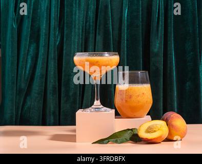 Frischer reifer Pfirsichfruchtsaft in einem Glas auf einem modernen abstrakten Podest und vor einem Hintergrund aus grünem Samtvorhang. Gesunder Lebensstil und richtige n Stockfoto