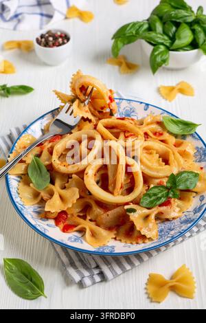 Hausgemachte Pasta Farfalle mit Tintenfisch in Tomatensauce, serviert mit frischem Basilikum, selektive Schärfentiefe Stockfoto