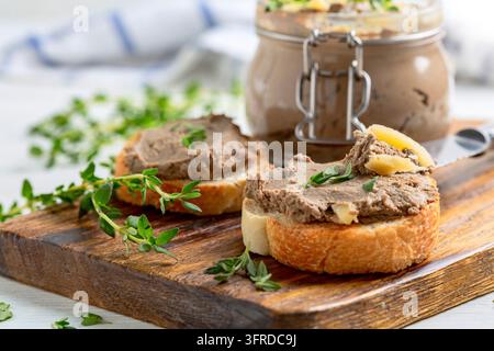 Scheiben gerösteten Baguettes mit Truthahnpastete mit Thymian und ein Glas Pastete werden auf einem hölzernen Servierteller serviert. Konzept von köstlichem hausgemachtem Essen Stockfoto