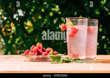 Getränk aus reifen roten Himbeeren in zwei durchsichtigen Gläsern, Sommerhintergrund. Sommerliches, frisch zubereitetes, erfrischendes Getränk, heller sonniger Tag, Licht Stockfoto