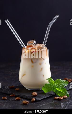 Kaltes frisches thailändisches Eiscafé serviert mit Milch und Glasstrohhalm mit Eiswürfeln auf Schieferplatte und schwarzem Hintergrund. Kopierraum. Konzept von kalten Getränken Stockfoto