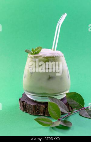 Glas kalter grüner Matcha-Tee gemischt mit Eiswürfeln und Milch auf einem Holzständer. Kopierraum. Konzept von eisgekühlten Sommergetränken Stockfoto