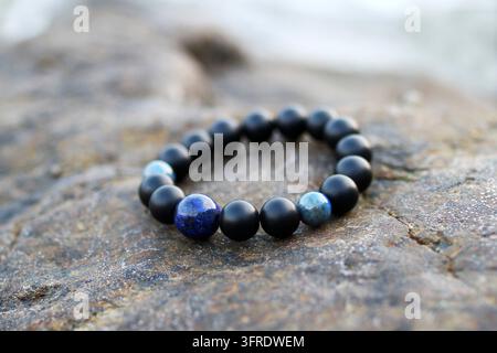 Armreif aus Natursteinen - schwarzer Achat und blauer Lazurit auf einem Hintergrund aus Felsen. Handgefertigter wertvoller Artikel. Schmuckaccessoires Stockfoto