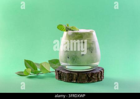 Eisgekühlter grüner Matcha-Tee gemischt mit Eiswürfeln und Milch in einem Latte-Glas auf grünem Hintergrund. Konzept eines eisigen Sommergetränks Stockfoto