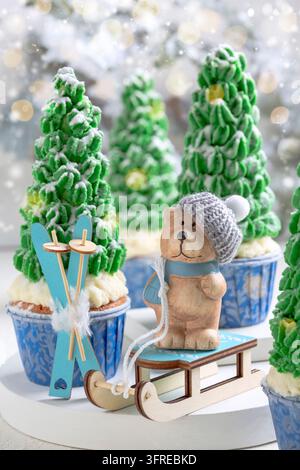 Weihnachts- oder Neujahrsspielzeug vor dem Hintergrund grüner Cupcakes, die mit aus Sahne gefertigten Weihnachtsbäumen verziert sind. Konzept der Weihnachtswinterferien Stockfoto