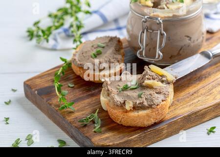 Scheiben gerösteten Baguettes mit Truthahnpastete mit Thymian und ein Glas Pastete werden auf einem hölzernen Servierteller serviert. Konzept von köstlichem hausgemachtem Essen Stockfoto