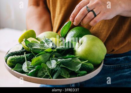 Eine Frau hält in ihren Händen frisches grünes Gemüse und Obst auf einem großen Teller, Nahaufnahme mit weichem Fokus. Vegetarismus gesunde Lebensweise ausgewogene Ernährung Nahrung r Stockfoto