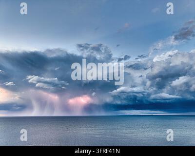 Ein mächtiger Blitz erhellt einen dunklen, stürmischen Himmel über der weiten Weite des Ozeans. Starker Regen strömt von bedrohlichen Kumulonimbuswolken herab Stockfoto
