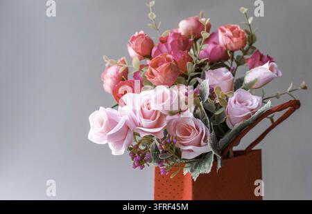 Blumenreihe. Rosa und rote Rosen in einer roten Schachtel auf grauem Hintergrund Stockfoto