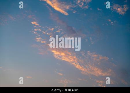 Leuchtend orangefarbene Sonnenuntergangswolken, die sich über einen tiefblauen Himmel verteilen und eine farbenfrohe natürliche Wolkenlandschaft und eine stimmungsvolle Hintergrundkulisse schaffen. Stockfoto