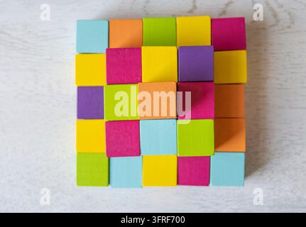 Eine Ansicht von oben zeigt kleine Holzwürfel in Zyan, Orange, Grün, Gelb, Rosa und Lila, die in einem ordentlichen quadratischen Raster angeordnet sind, um ein farbenfrohes mosaikähnliches Muster zu bilden Stockfoto