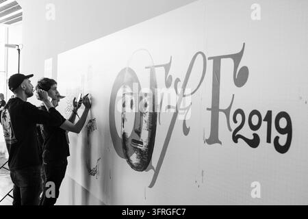 TEAM VON KÜNSTLERN BEI DER ARBEIT IN SCHWARZ-WEISS, BARCELONA OFFF FESTIVAL 2019 REPORTAGE, BARCELONA, SPANIEN: In Schwarz-Weiß aufgenommen, zeichnen zwei Männer eine große Wandgrafik, während ein anderer sie mit einem Telefon filmt oder fotografiert. INFO: Die OFFF-Konferenz wurde 2001 ins Leben gerufen und ist die weltweit größte Plattform für zeitgenössische visuelle Kreativität und Design. Sie zieht die besten Designer, Künstler, Filmemacher und Fotografen der Welt an. Sie dient als globale Plattform für kreativen Austausch und Zusammenarbeit. Stockfoto