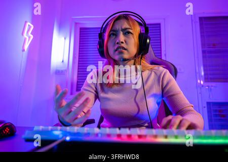 Spiel vorbei. Wütender asiatischer Gamer trägt Gaming-Kopfhörer und spielt Videospiel auf dem Computer-PC mit violettem Licht in der Nacht zu Hause, weiblich, müde und traurig Stockfoto