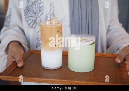 Zwei Getränke auf einem Holztray, gehalten von einer Person in einem hellen Outfit Stockfoto