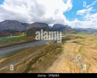 Hochwinkel-Luftaufnahme von sanften Hügeln und Ackerland, die zu einem breiten Flussbett und hoch bewölkten Bergen führen Stockfoto