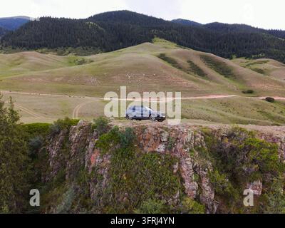 Almaty-Region, Kasachstan – 10. Oktober 2023: Luftaufnahme eines Autos, das am Rand einer felsigen Klippe geparkt ist und grüne Hügel sowie Nadelwald überblickt Stockfoto