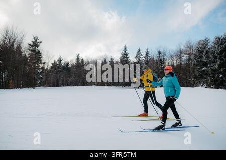 Aktives Paar lädt Langlaufski durch verschneite Landschaft während des Winterurlaubs. Stockfoto