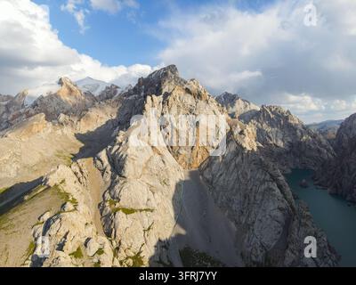 Luftbild von schroffen felsigen Berggipfeln und Geröllhängen, die von Sonnenlicht unter Wolken beleuchtet werden Stockfoto