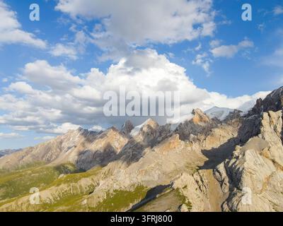 Luftaufnahme von schroffen felsigen Berghängen und grünen Kämmen, die zu entfernten schneebedeckten Gipfeln führen Stockfoto
